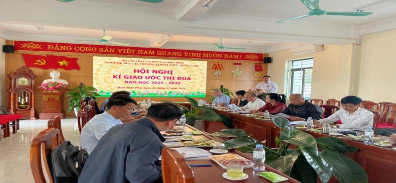 '''A group of people sitting at long tables in a room with a screen
Description automatically generated'''